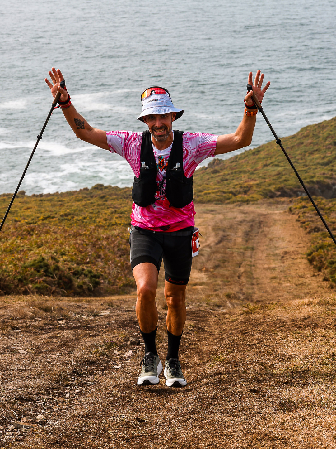 An ultradistance participant raises both hands on a coastal section of 21 Leguas Narón