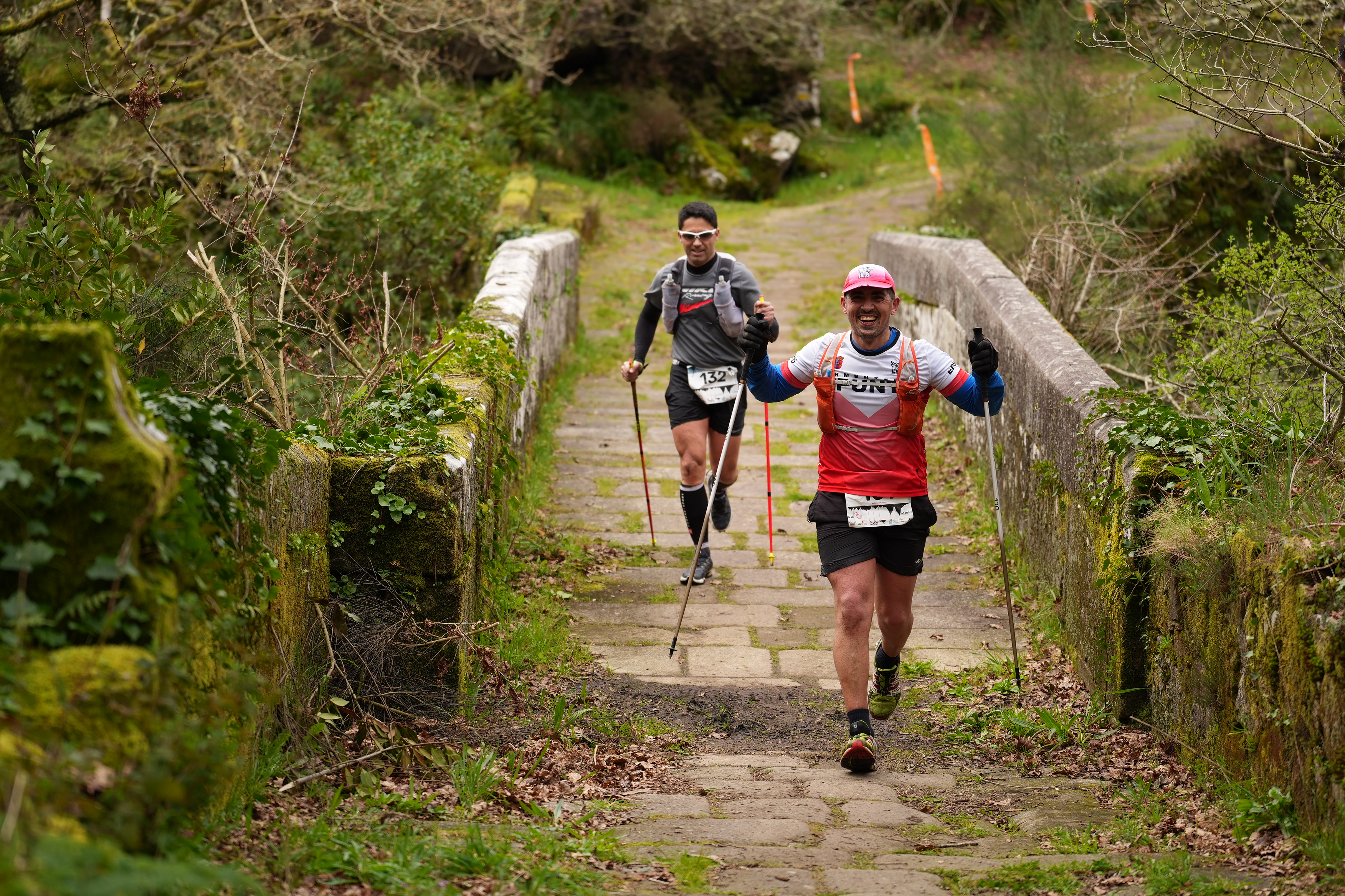 Two runners crossing an old stone bridge on the Laxe dos Bolos course
