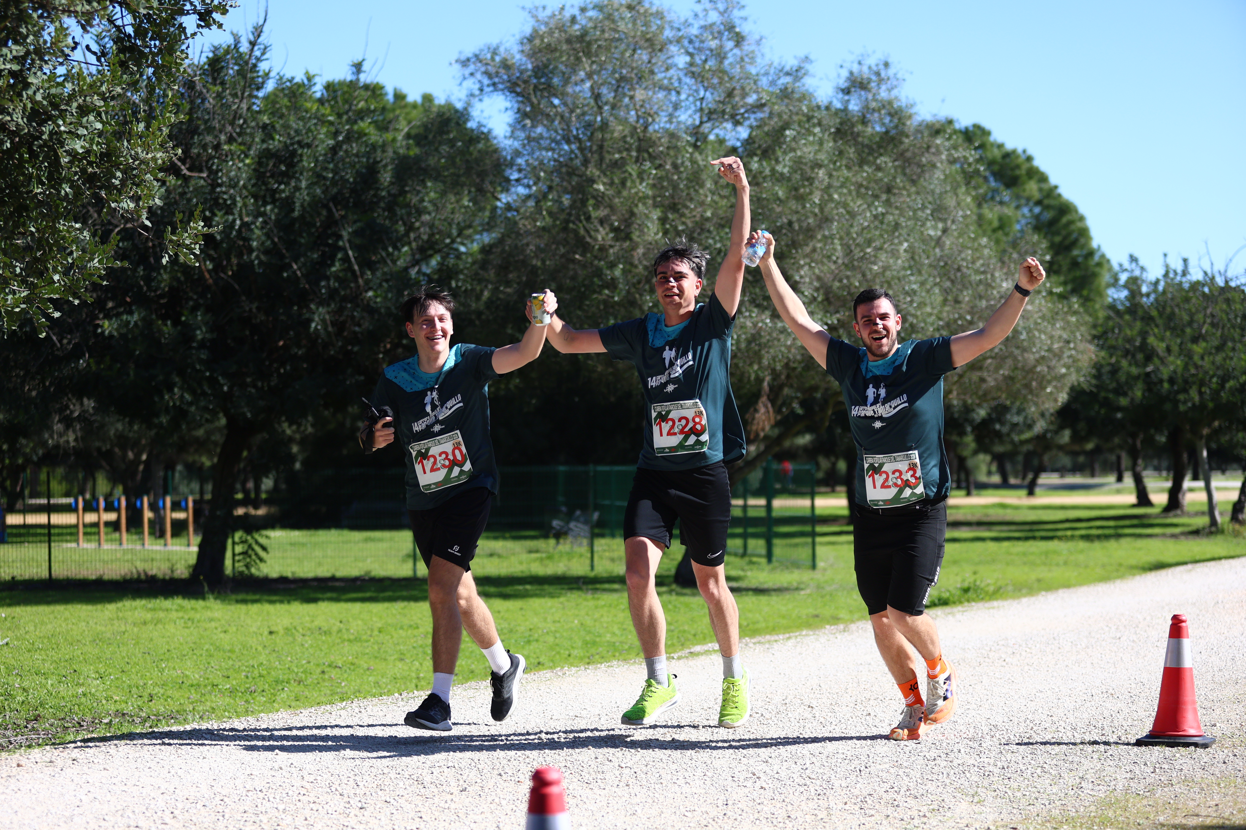 Three finishers raise their arms in celebration after crossing the line at Carrera Popular Parque Tamarguillo