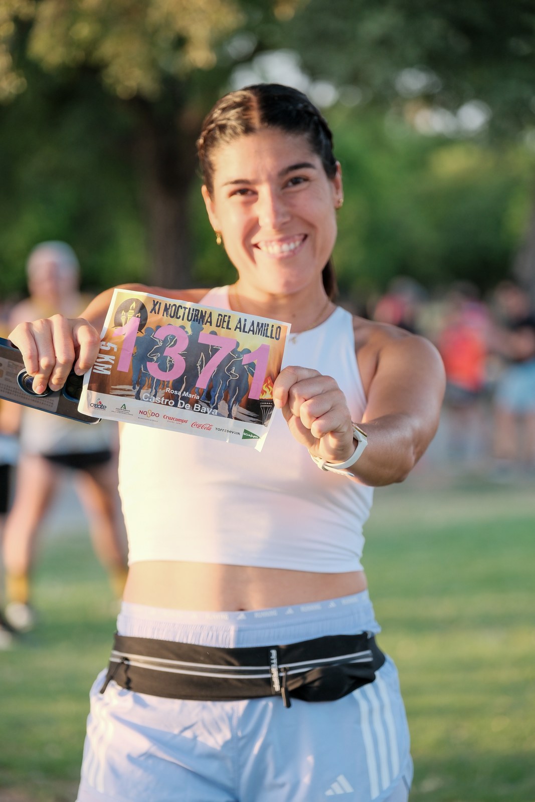 A runner holds up her XI Nocturna del Alamillo race bib after finishing the 5km race