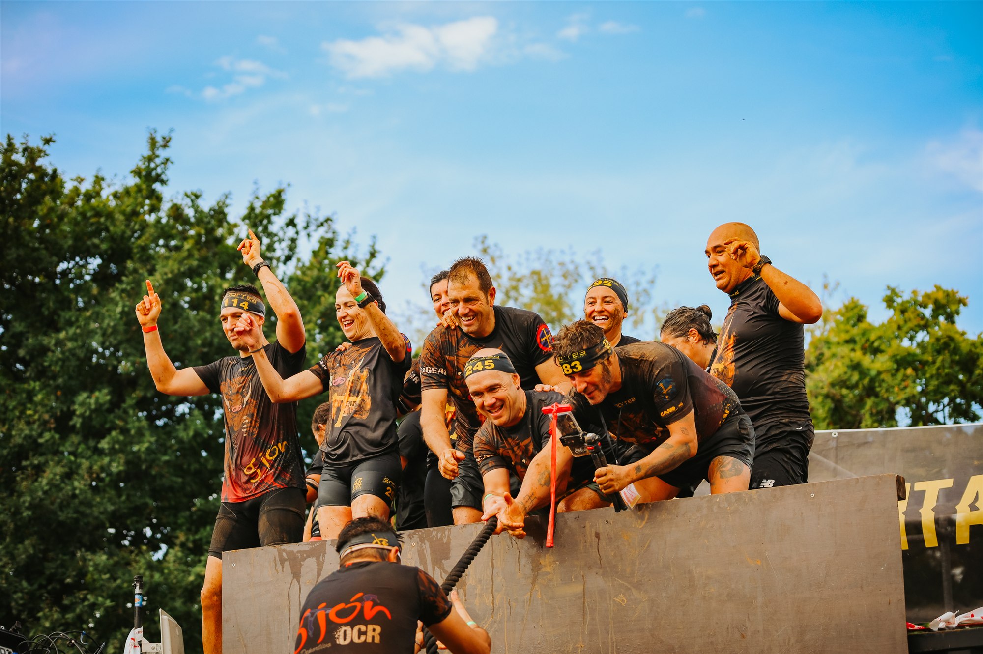 Mud-covered Cabárceno Race participants celebrate together at an obstacle