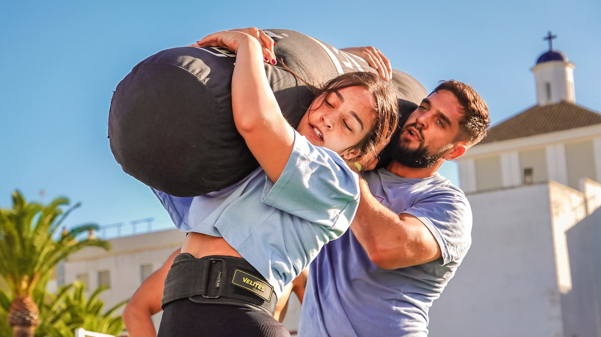 Two athletes share a weighted bag across their shoulders at Cádiz Throwdown
