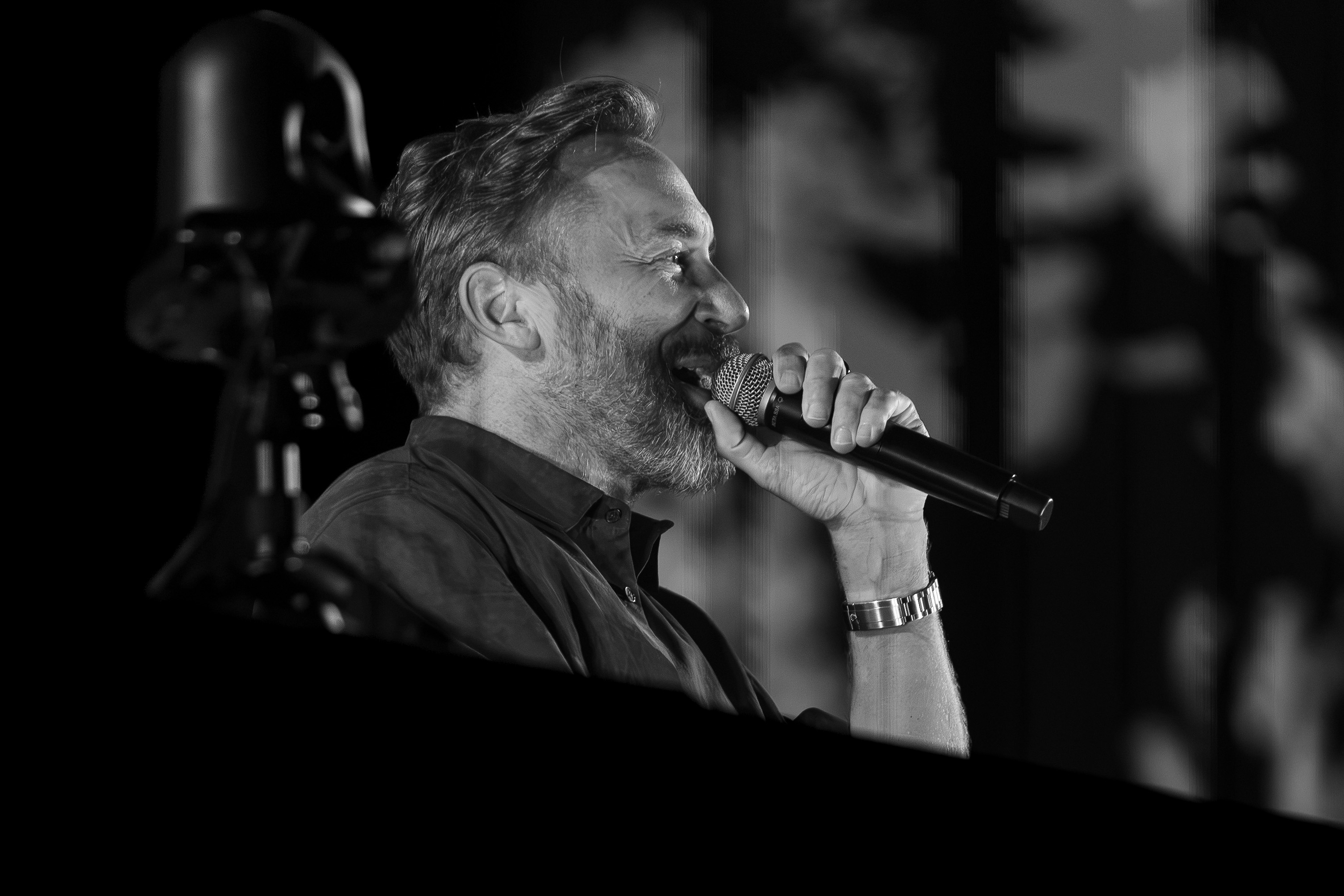 Black and white close-up of David Guetta speaking into a microphone on stage during The Monolith Tour in Loures