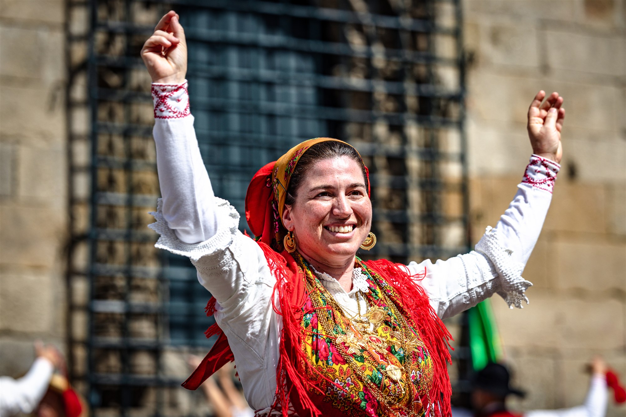 A smiling performer in traditional red-and-white dress during Fest’In Folk Corredoura in Guimarães
