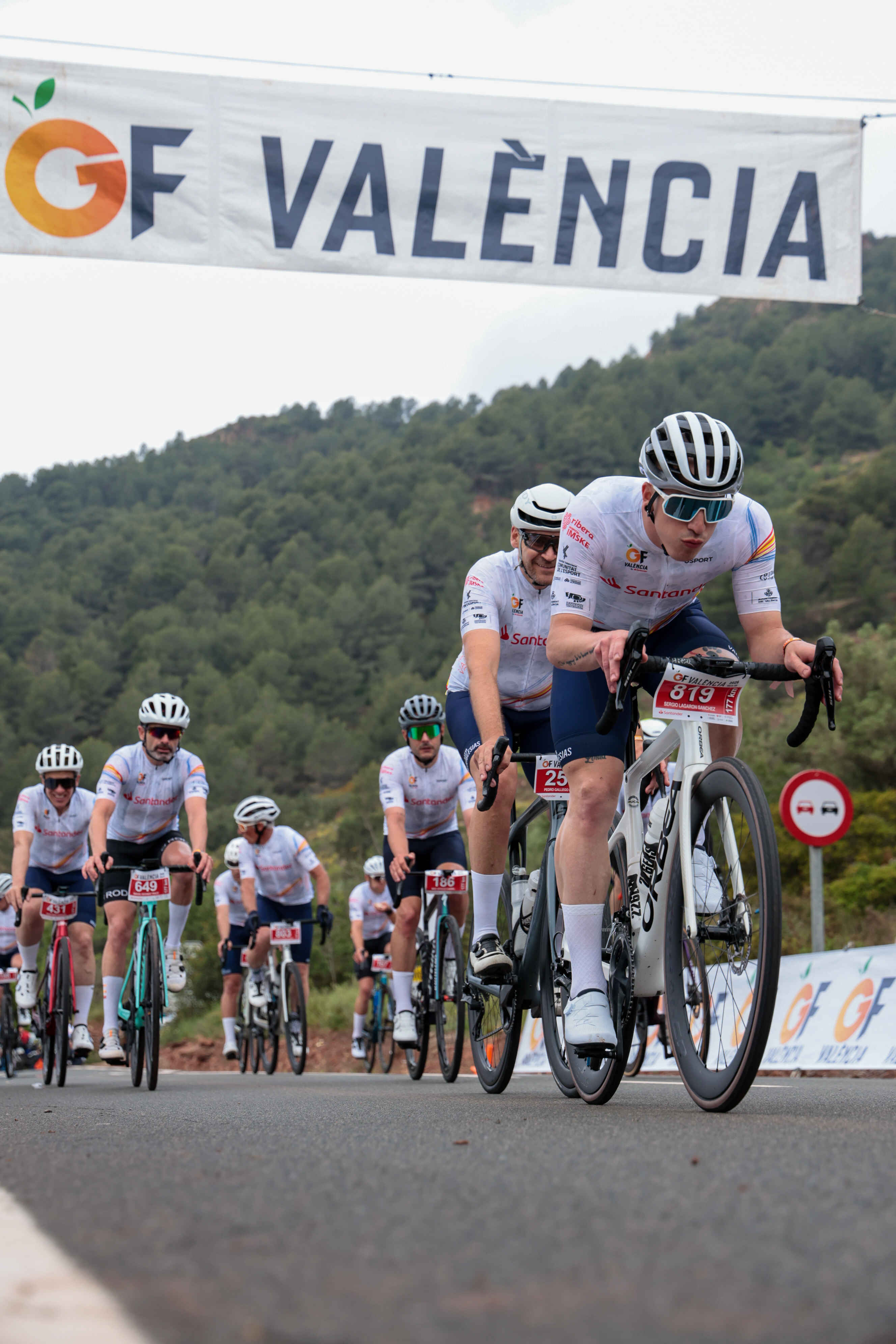 A group of cyclists climbing beneath the GF València banner