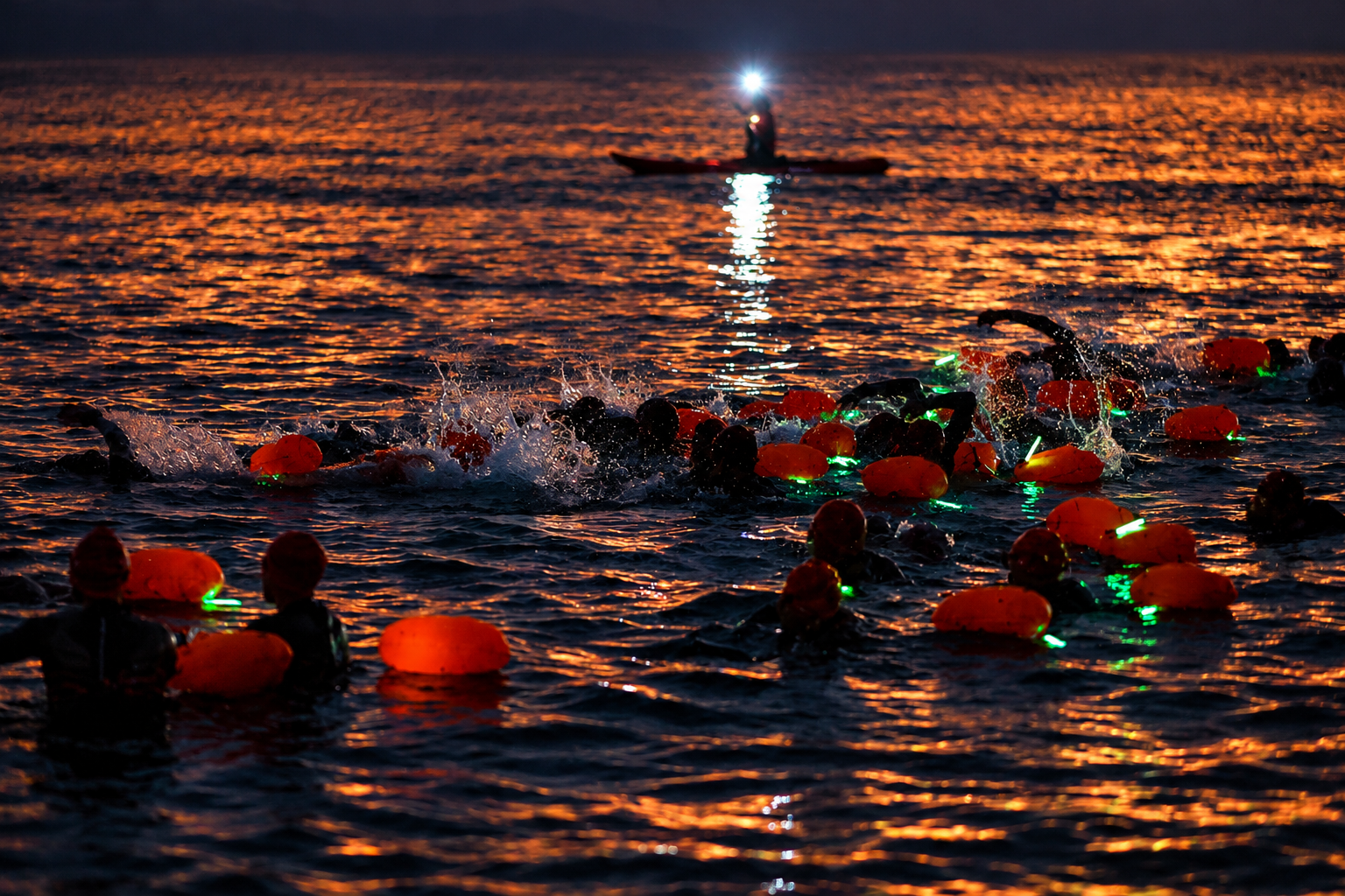 Swimmers and illuminated orange floats in dark water