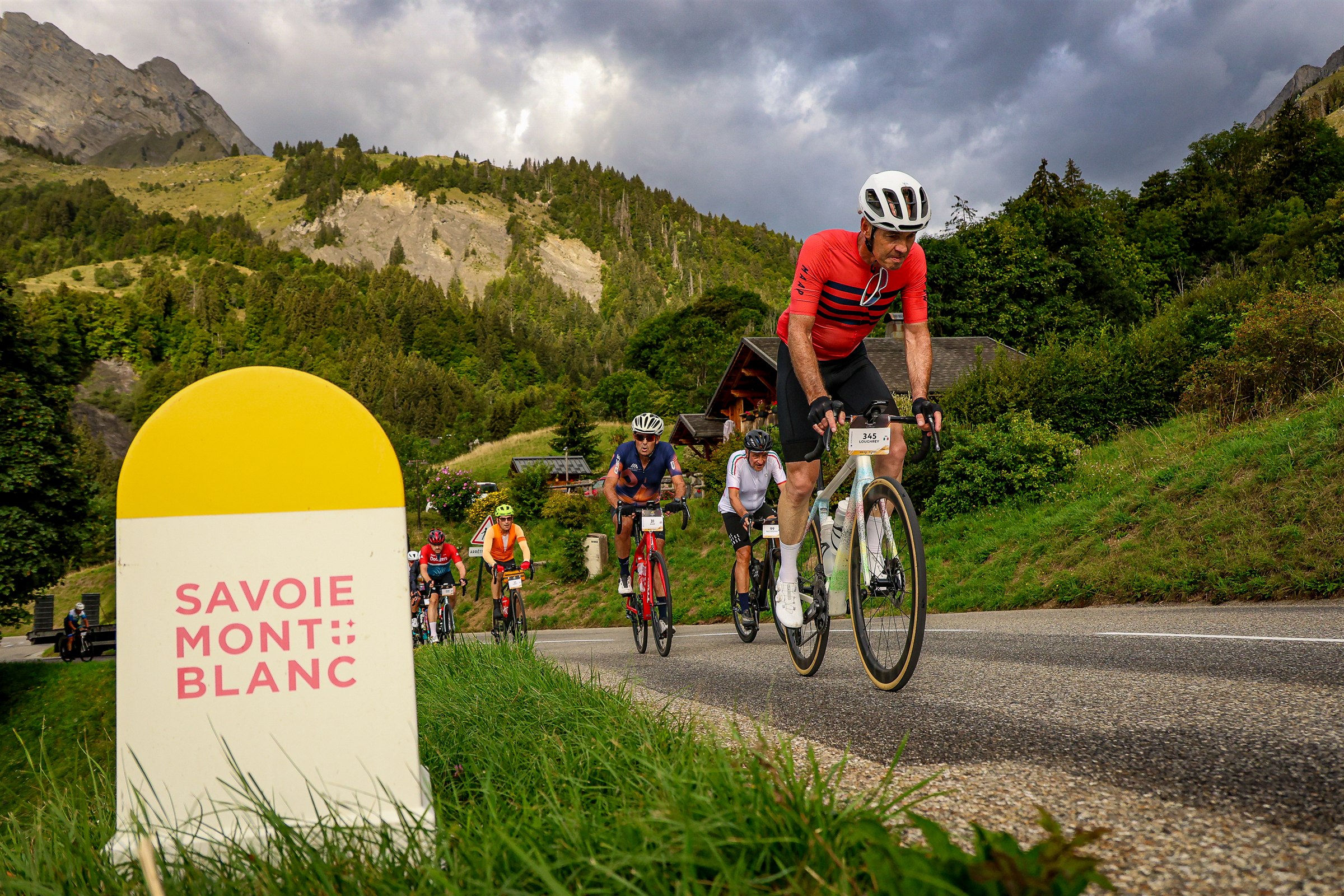 Cyclists climb through Savoie beneath dark Alpine clouds during Haute Route Alps 2026