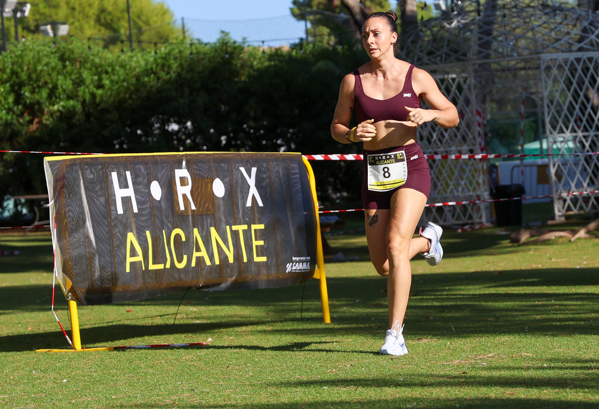 An athlete runs on grass beside an HRX Alicante sign