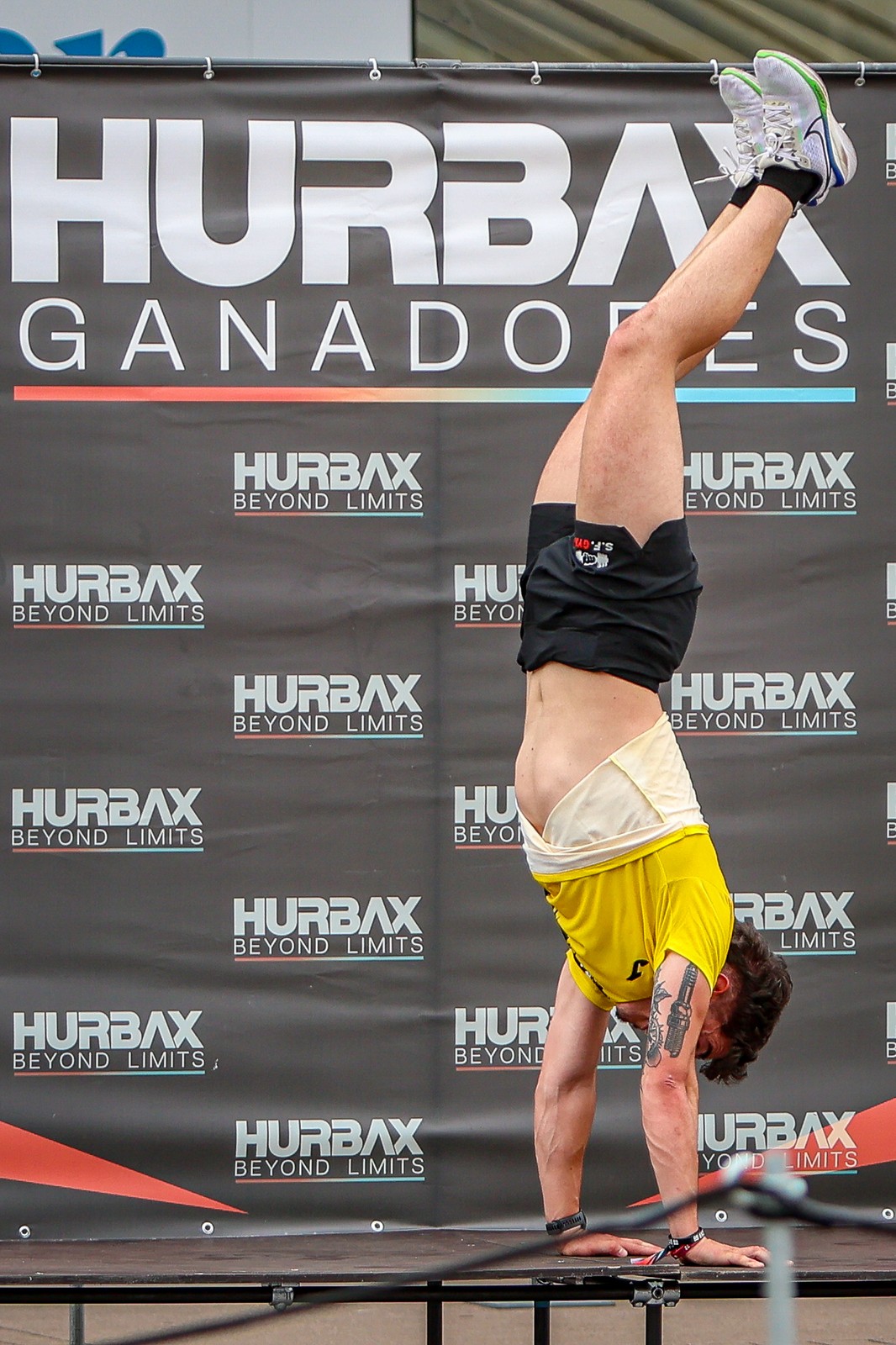 An athlete performs a handstand on the winners' podium at Hurbax Oviedo