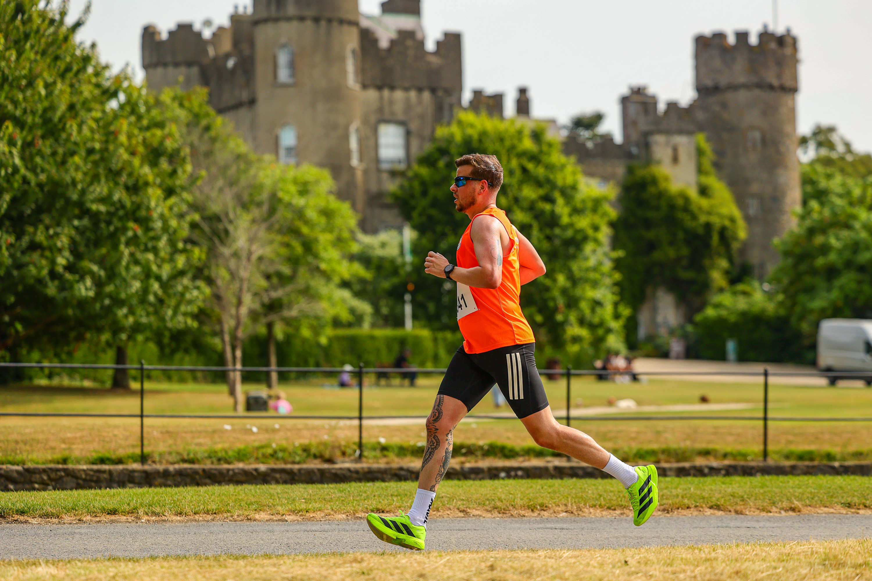 A runner in an orange singlet passes Malahide Castle's twin towers in the background during the Malahide Castle 10km