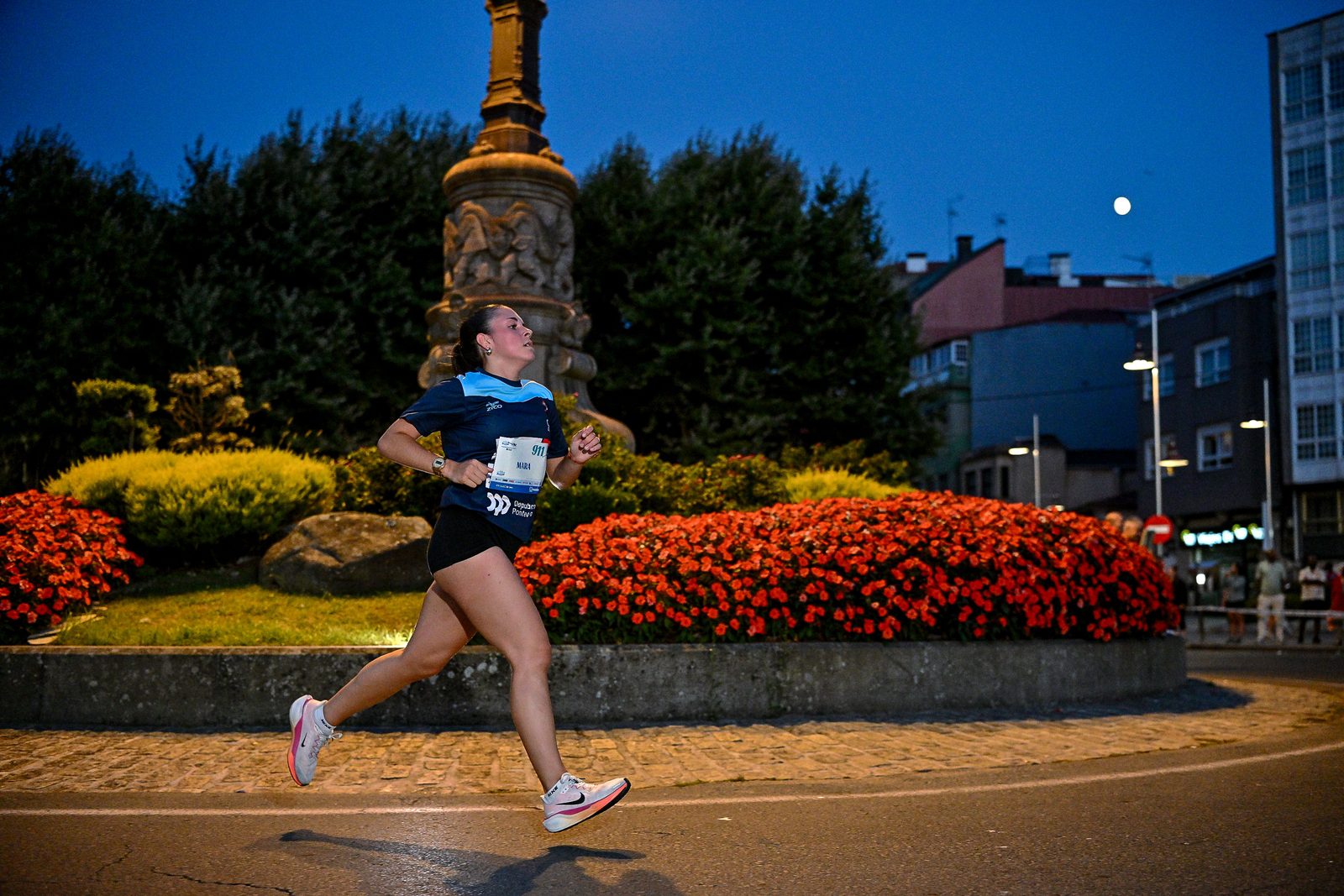 A runner passes an illuminated fountain and flowerbeds after dark during the Manuel Rosales +10 Marín