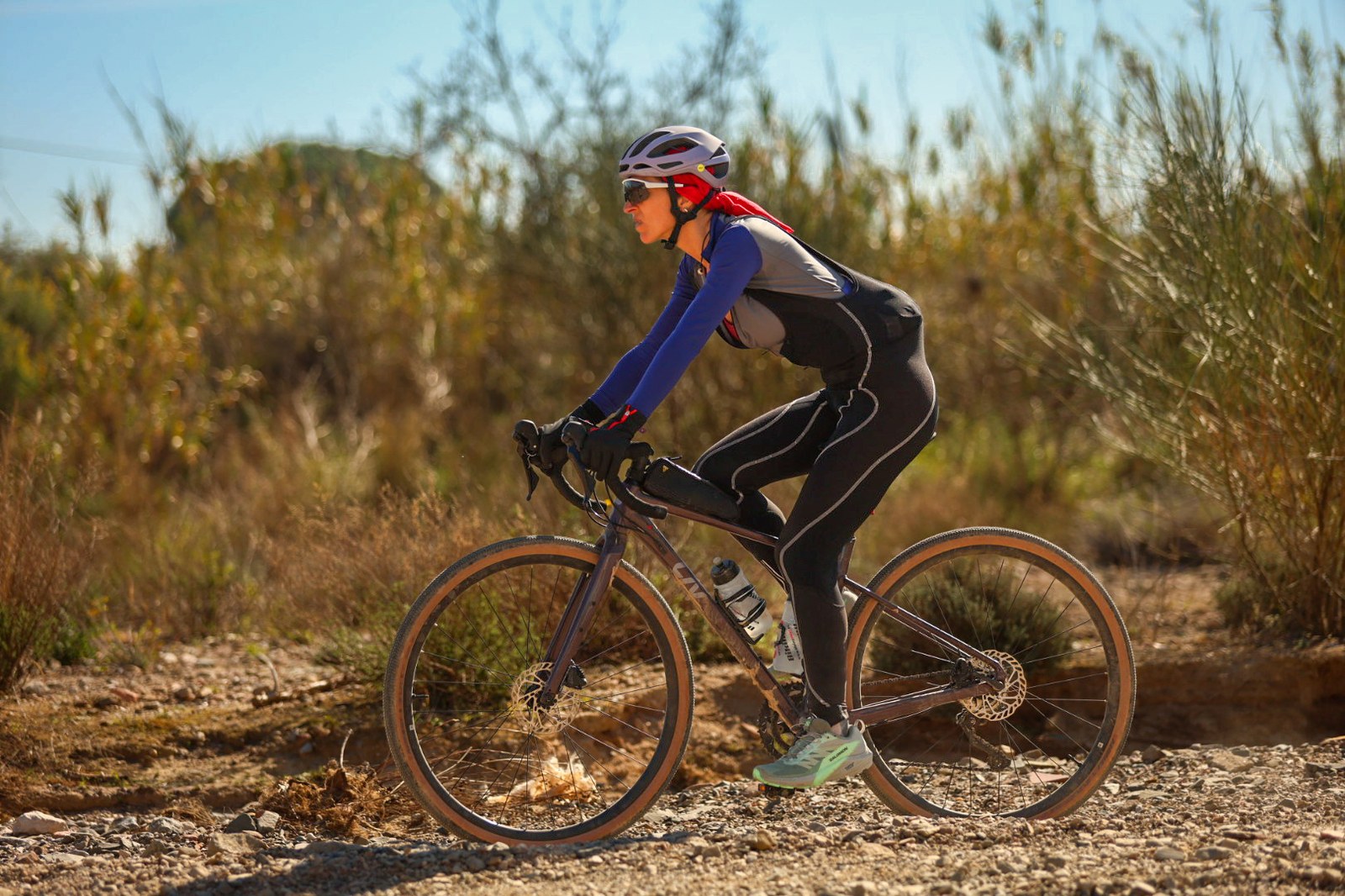 A cyclist in gravel-riding gear rides through dry scrubland terrain during Massos Gravel