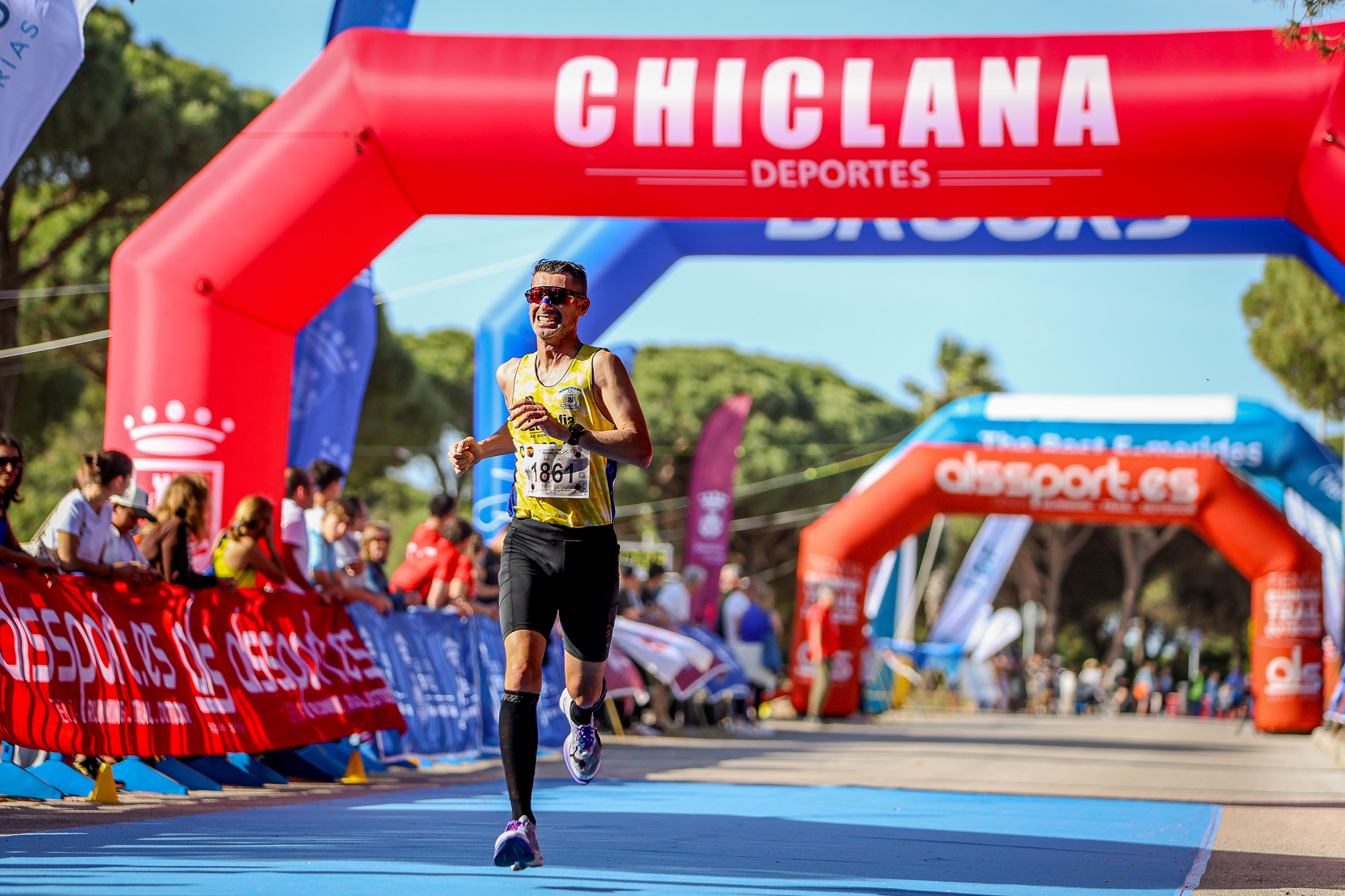 A runner crossing the finish line under the Chiclana Deportes arch at the III Viamed Media Maratón Ciudad de Chiclana