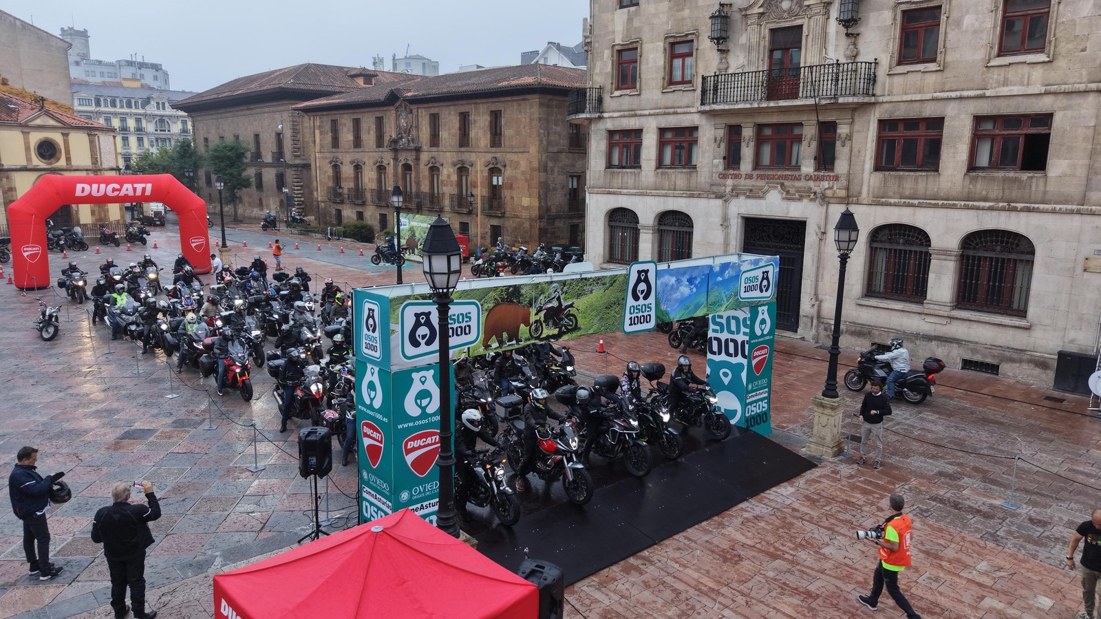 Riders line up on wet pavement at the OSOS 1000 start podium in Oviedo on the morning of the ride