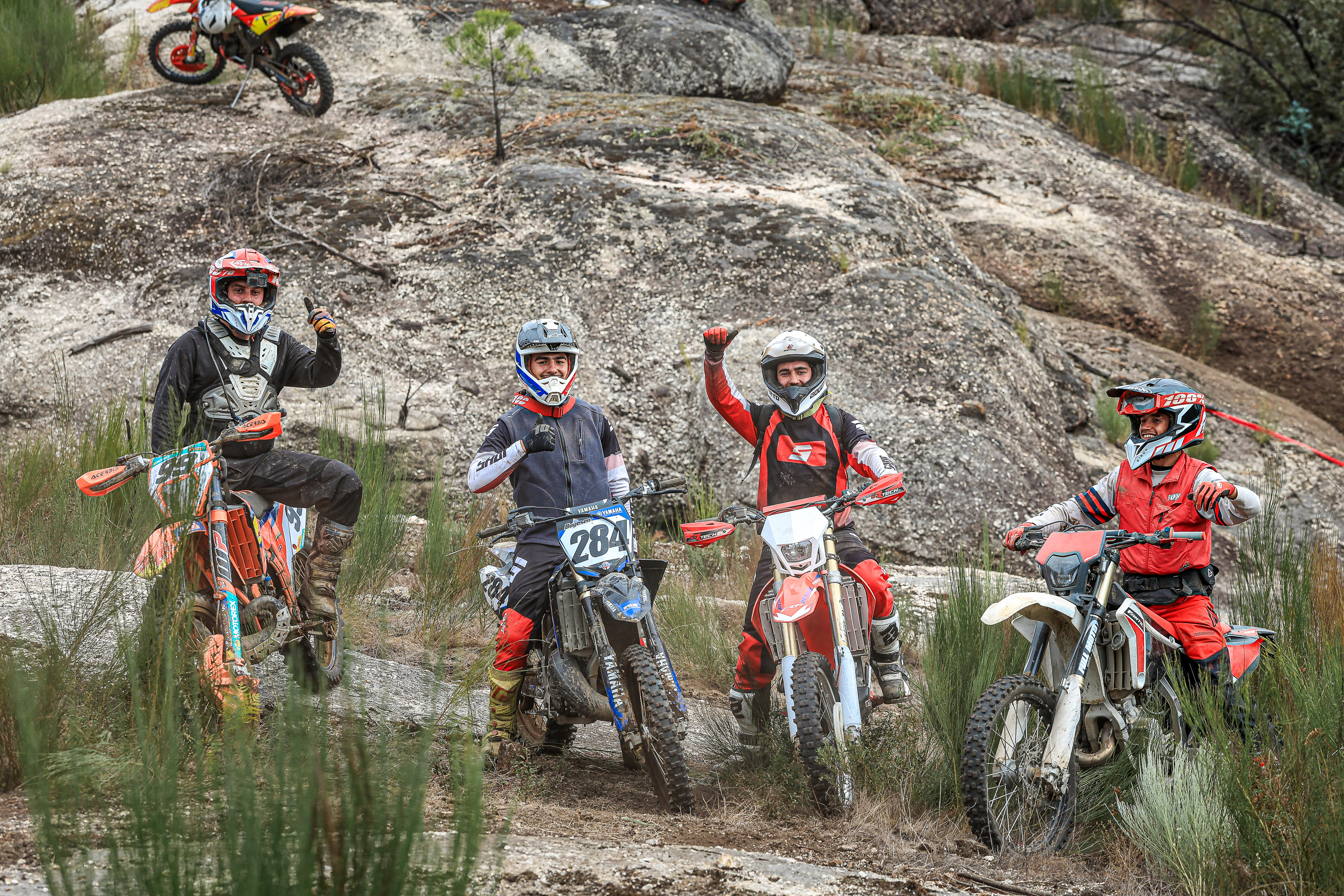 Four off-road motorcyclists gather together on rocky terrain