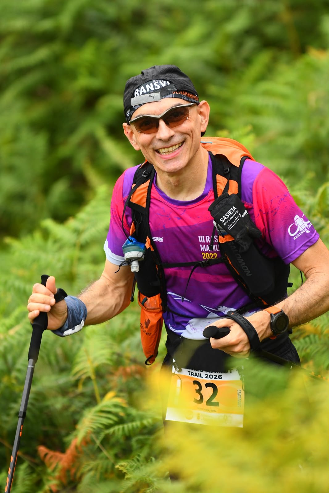 A competitor uses trekking poles on a fern-lined climb during Rasines Mamut Trail 2026