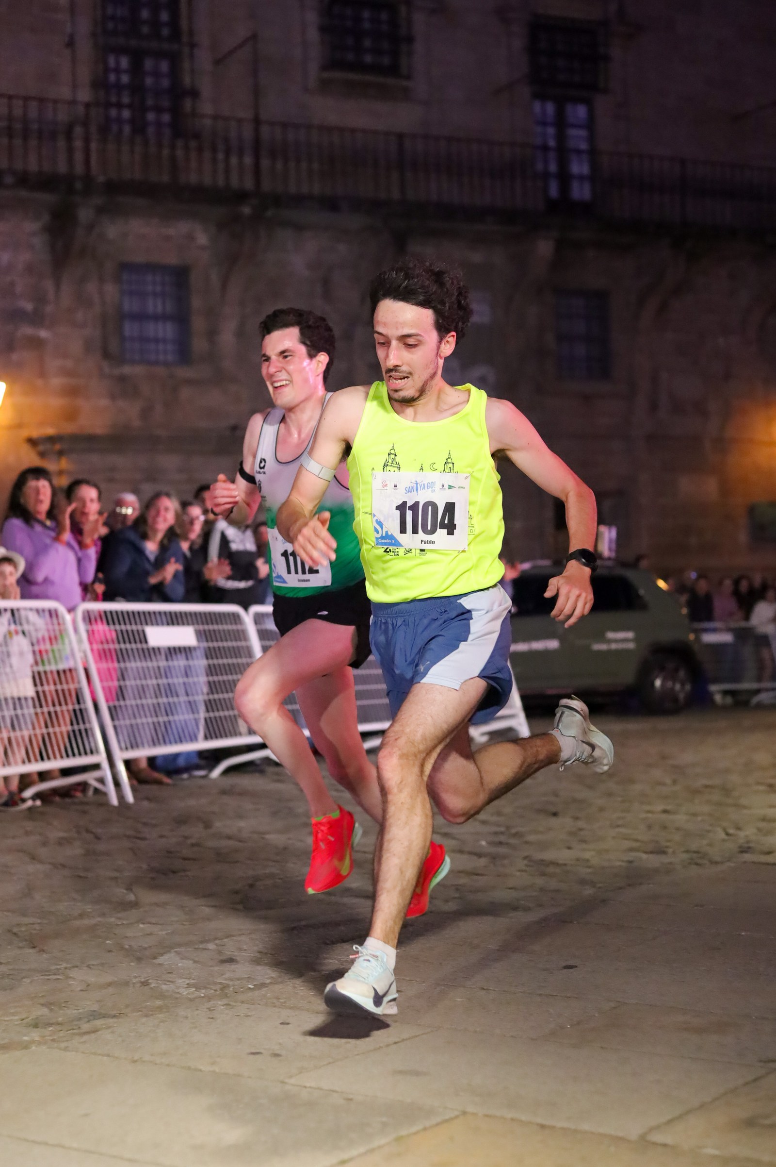 Two runners sprint for the finish line together at night during the SantYaGo10K in Santiago de Compostela