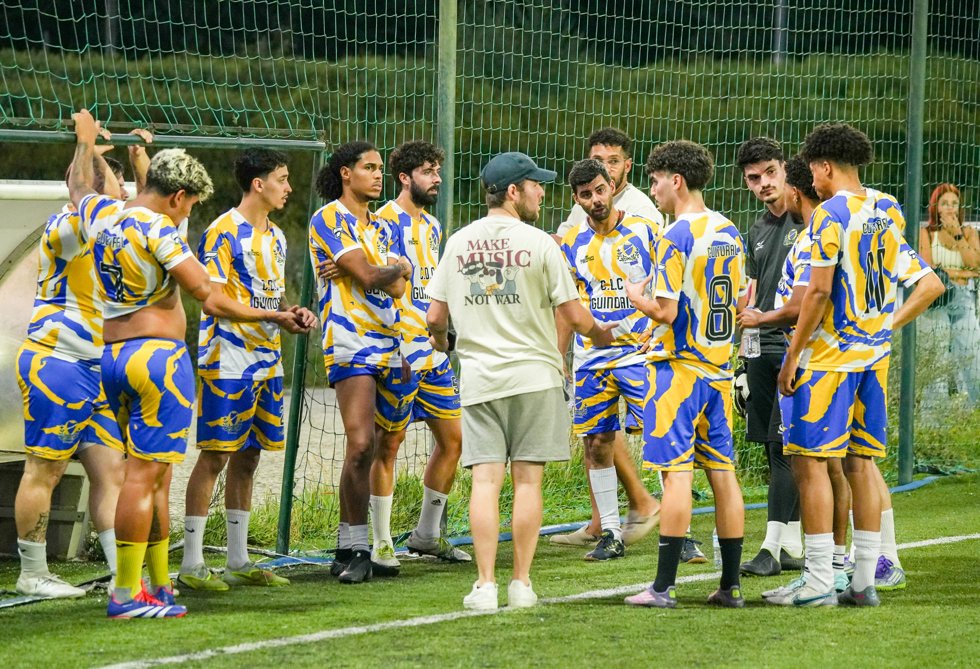 Players in blue, yellow and white gather beside the pitch at SOCCA Porto