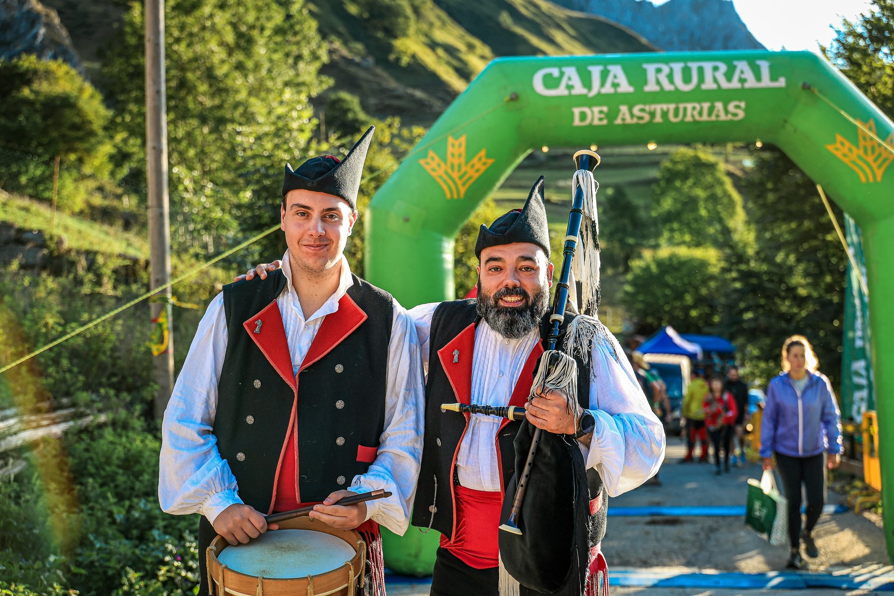 Two musicians in traditional Asturian dress stand near the Trail de Ubiña finish area