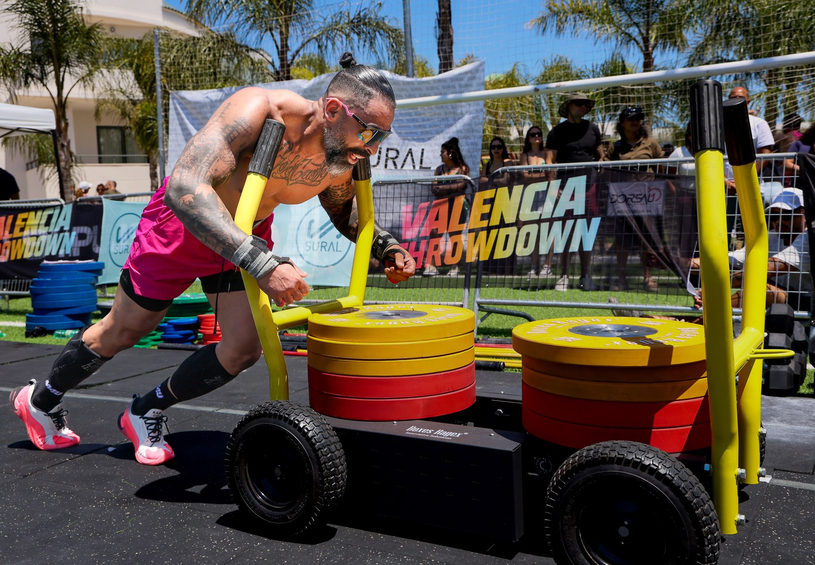 An athlete in pink shorts pushes a weighted sled past the Valencia Throwdown banner